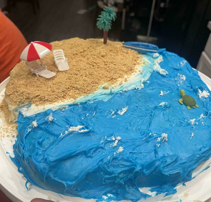A creative baker's delicious treat: a cake designed as a beach scene with blue waves, sand, and tiny beach accessories.
