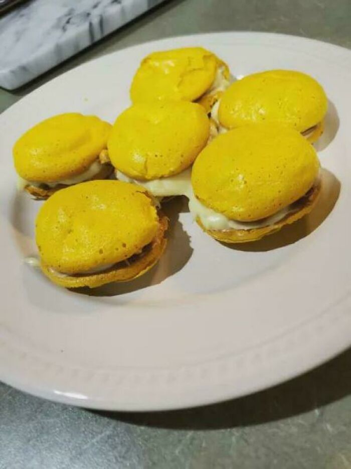 A plate of yellow macaron treats with creamy filling, proving bakers make delicious and amazing desserts.