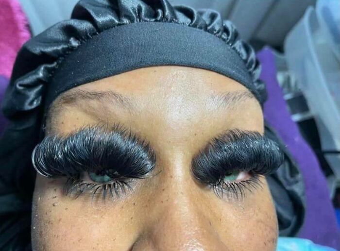 A person with extremely long and dense eyelash extensions from a beauty salon, looking significantly worse.