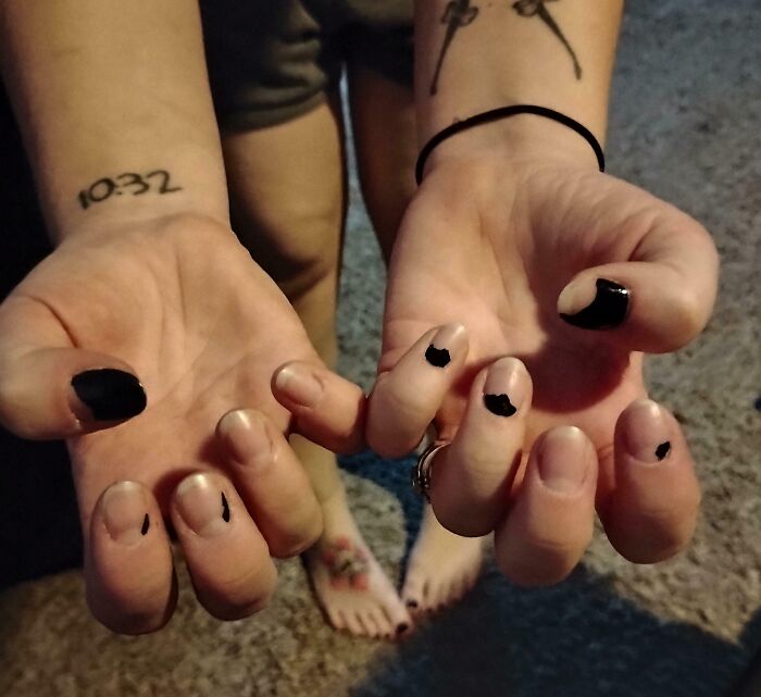 A person's hands with poorly applied black nail polish and a tattoo of 10:32 on their wrist, showing a beauty salon fail.