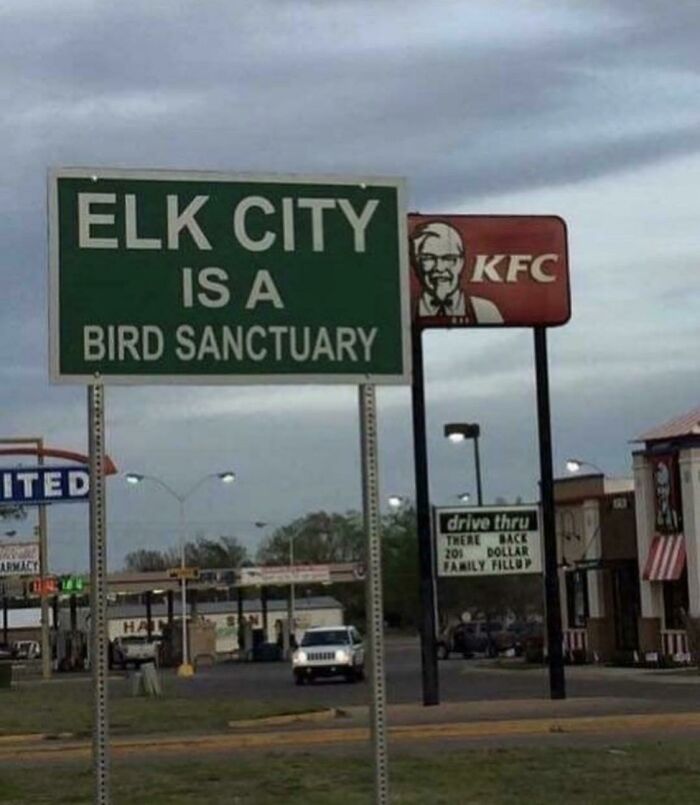 Green sign says Elk City is a bird sanctuary near KFC restaurant irony