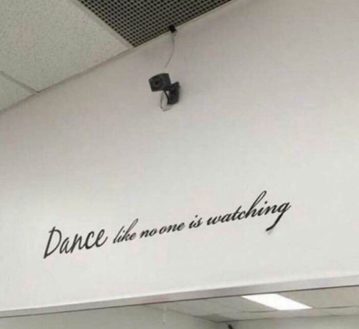 Wall sign says dance like no one is watching under visible surveillance camera