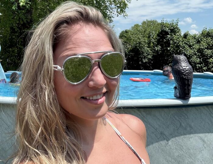 Woman wearing reflective sunglasses by a backyard pool on a sunny day