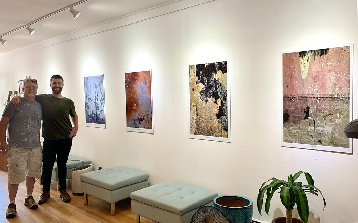 Two amazing fathers posing proudly with abstract art on a gallery wall, reflecting their supportive parent roles.