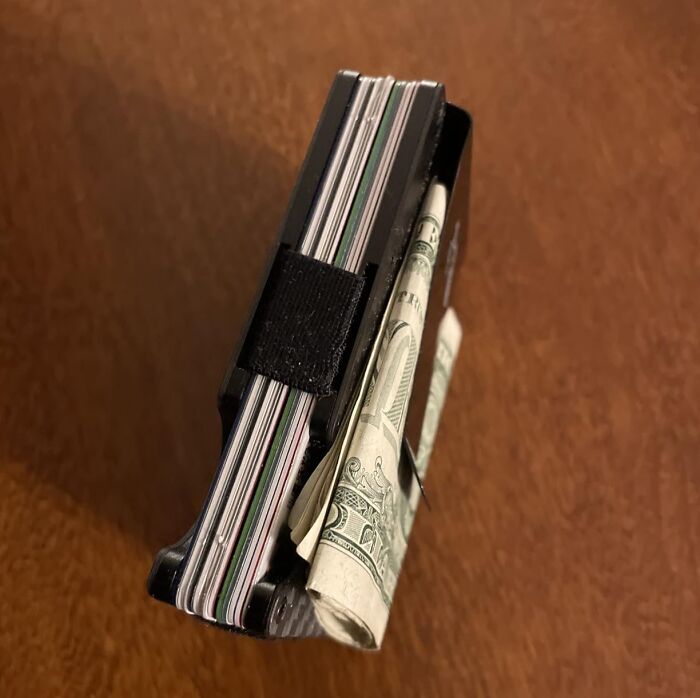 A black minimalist wallet holding cards and cash, a practical last minute Fathers Day gift idea.