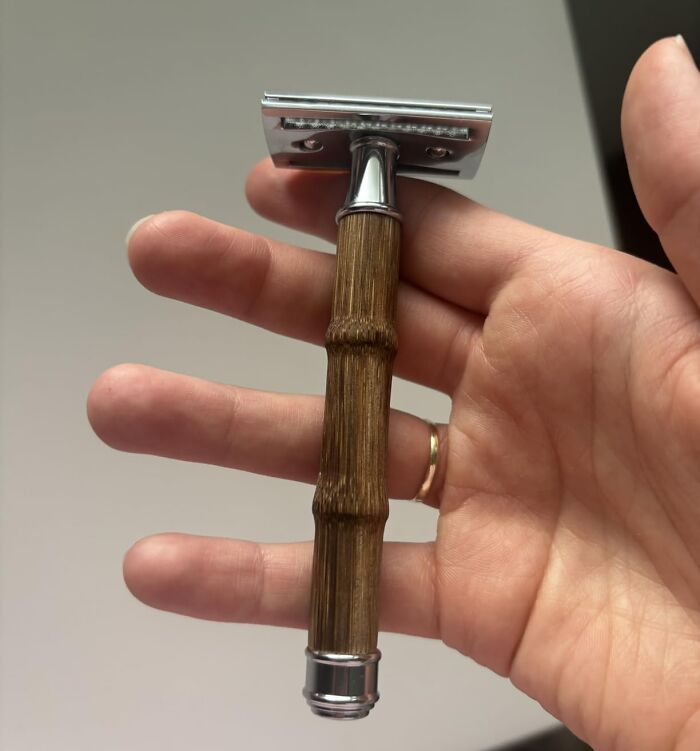 A hand holding a classic safety razor with a bamboo handle, a last minute Father's Day gift.