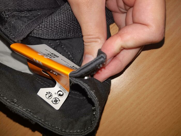 A hand struggling to remove a tag from black pants, highlighting a bad clothing design.