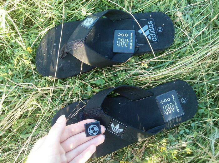 A pair of black sandals with adidas branding and a soccer ball logo, displaying bad clothing designs on grass.