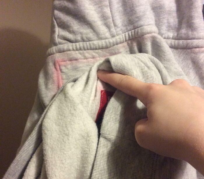 A hand pointing to a poorly stitched pocket on a grey hoodie, illustrating a bad clothing design.