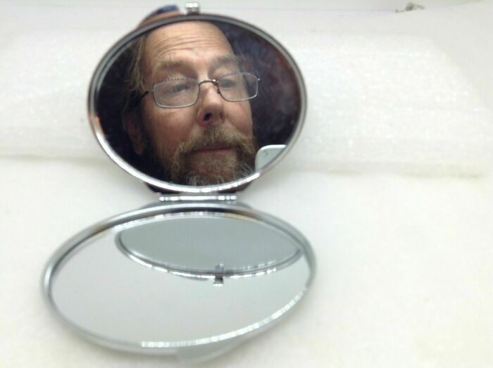 An amazing father with a beard and glasses reflected in a compact mirror, showcasing his unique personality.