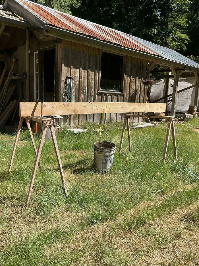A wooden beam balanced on two sawhorses, with a bucket hanging from it, demonstrating clever solutions.