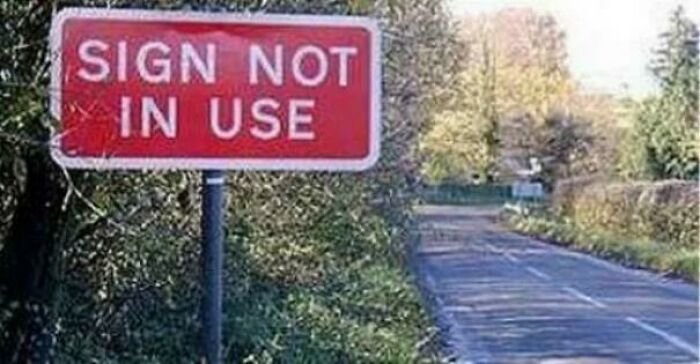 A red sign reading 'SIGN NOT IN USE' on a pole beside a road, one of many baffling images.