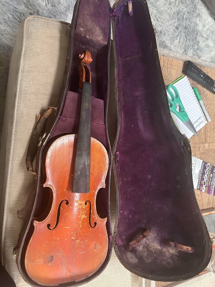 An old wooden violin in a purple-lined case, representing rare old treasures discovered by antique lovers.