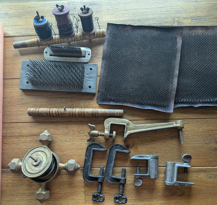 Assorted old treasures including spools, clamps, and carding tools laid out on a wooden surface