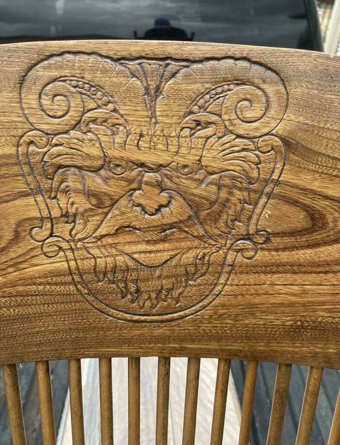 A detailed wood carving on an antique chair featuring a mythical horned face design