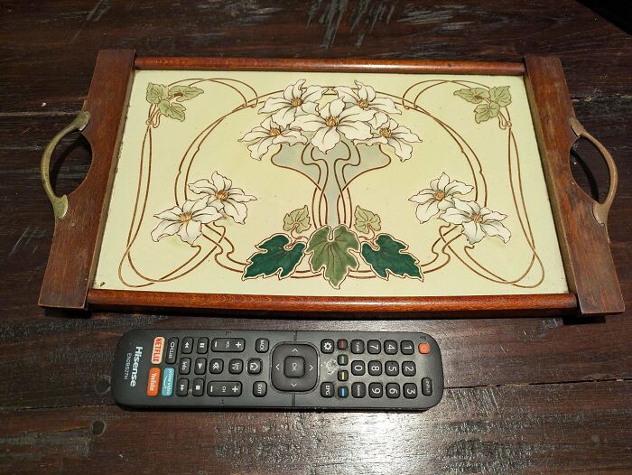 Art Nouveau floral wooden tray next to a modern TV remote, displaying unique old treasures found by antique lovers.