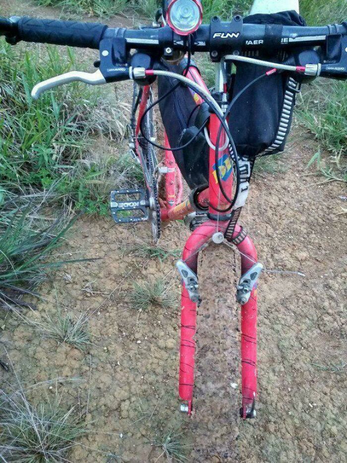 A bicycle with its front wheel missing, appearing like a glitch in the matrix on a dirt path.