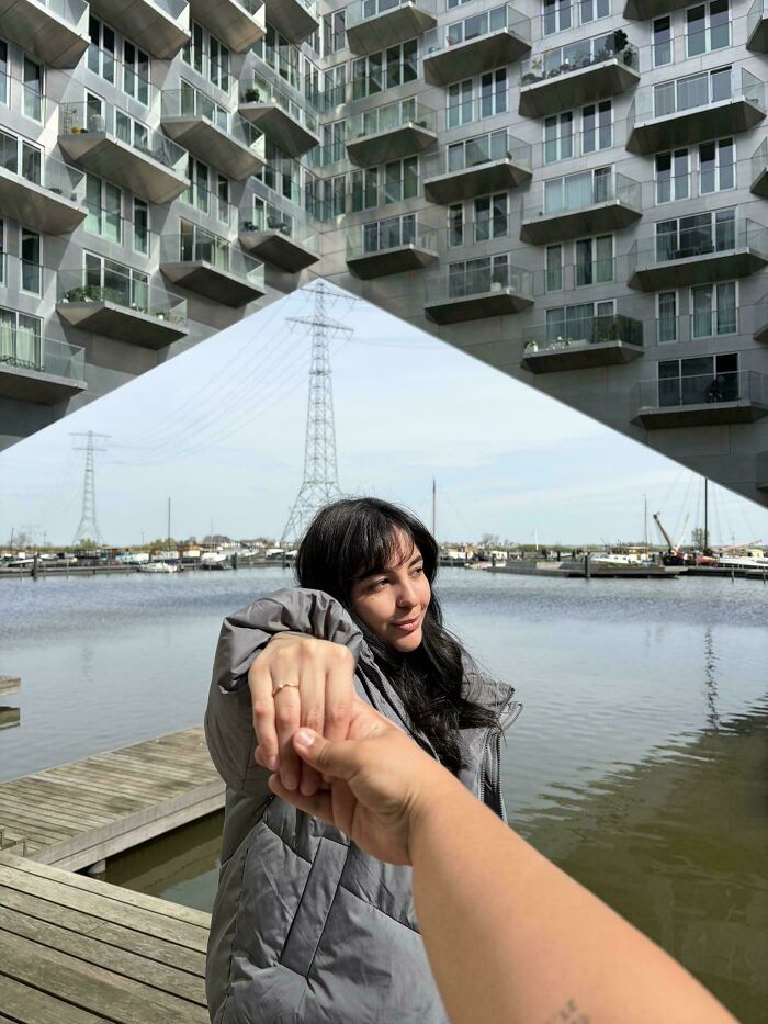 A woman holding hands with another person, with modern buildings and a lake in the background creating a glitch in the matrix effect.