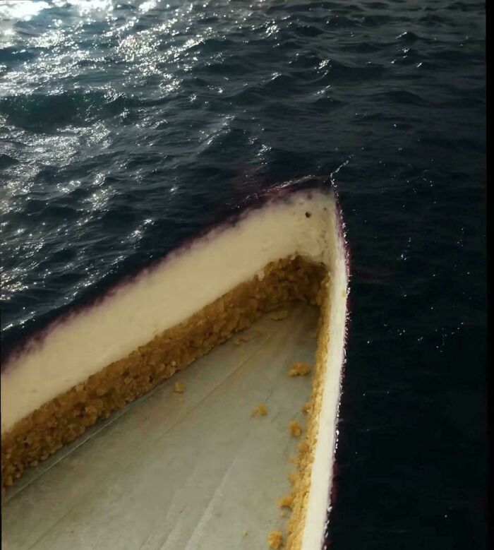 An optical illusion of a cheesecake slice floating on dark ocean water, a glitch in the matrix pic.