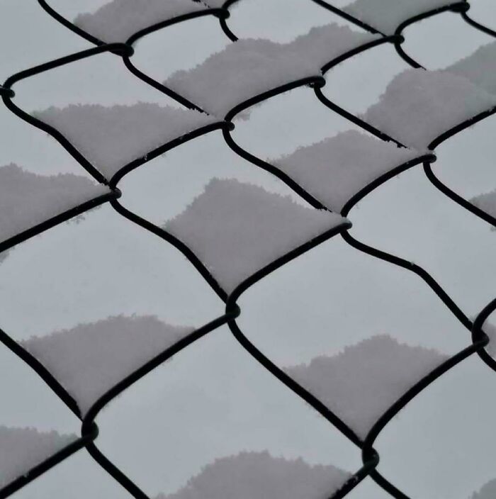 Snow on a chain-link fence, creating an optical illusion or a glitch in the matrix effect.
