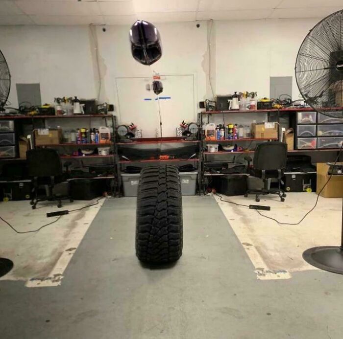 A tire standing upright in a workshop with a helmet hanging above, looking like a glitch in the matrix.