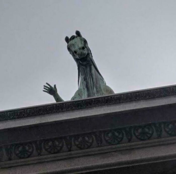 A horse statue with a human arm waves from a building roof, looking like a glitch in the matrix.