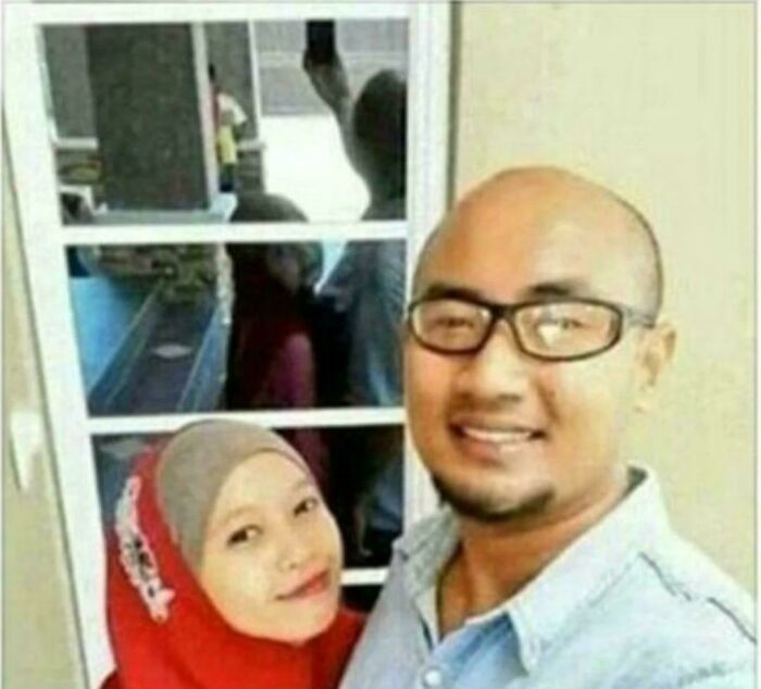 A couple smiling for a selfie, with a reflection in the window creating a Glitch in the Matrix effect.