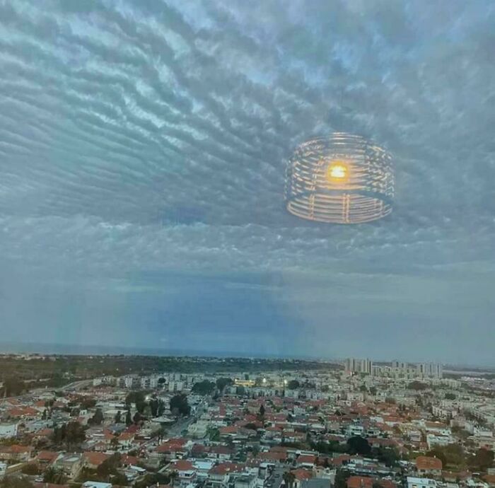 A cityscape under a cloudy sky with a floating, glowing structure that looks like a glitch in the matrix.