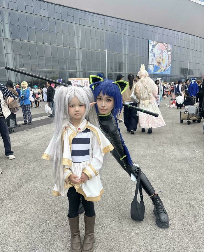 Two cosplayers at an outdoor event, one with long white hair and the other an optical glitch in the matrix illusion.
