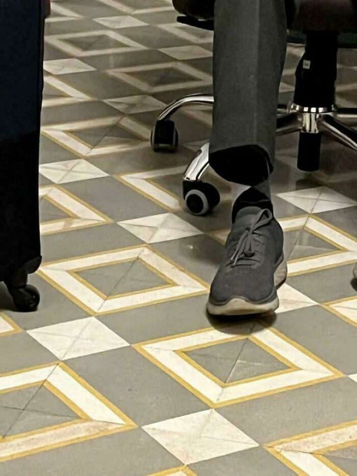 A persons foot wearing a grey shoe on a tiled floor that looks like a glitch in the matrix.