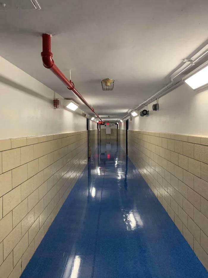 A long, empty school hallway with a blue floor, creating a perspective that looks like a glitch in the matrix.