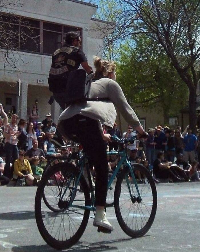 A woman on a bicycle carrying a man on her back, appearing like a glitch in the matrix.