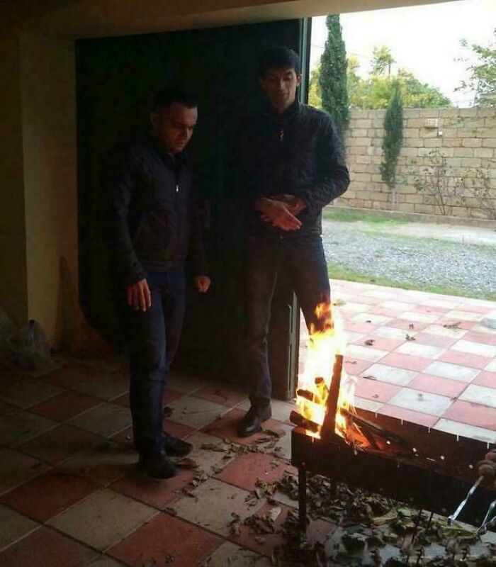 Two men standing near a grill with flames, creating an optical illusion, a glitch in the matrix.