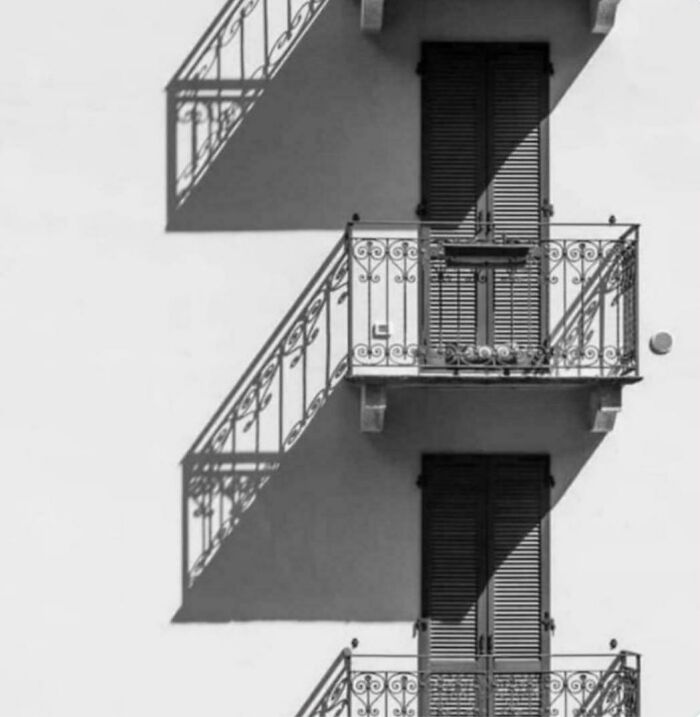 A black and white image of building balconies with strong shadows, creating a glitch in the matrix visual effect.