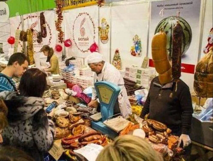 A market scene with various meats, and a man appears to have a large sausage as his head, a glitch in the Matrix.