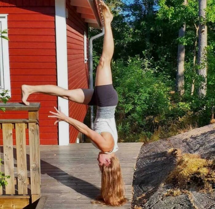 Woman in a handstand creating a Glitch In The Matrix, with one leg extended against a wooden railing.