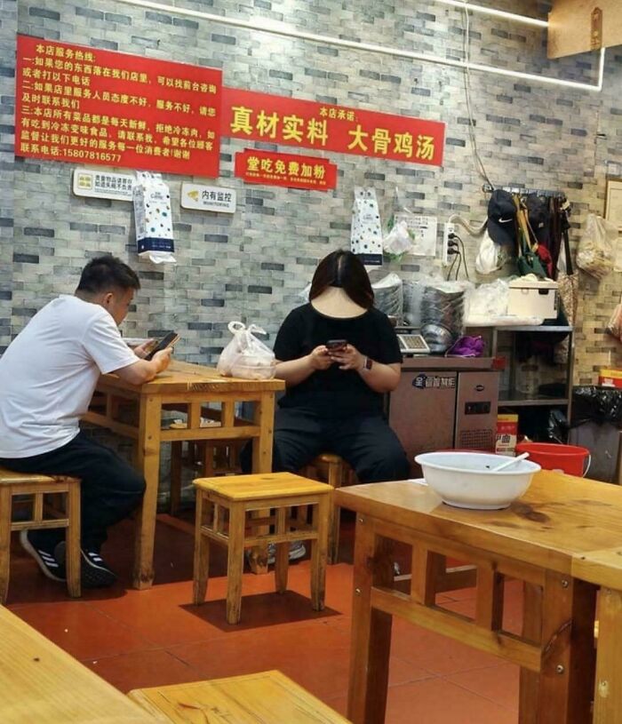 Two people in a simple restaurant, engrossed in their phones, creating a scene that looks like a glitch in the matrix.