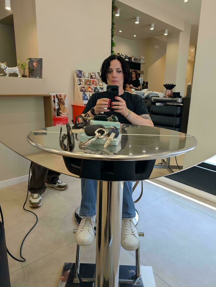 A woman sitting at a table in a salon, creating a glitch in the matrix with her reflection and objects on the table.