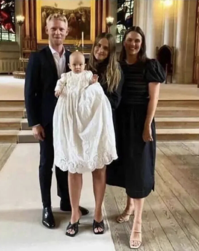 Three adults stand with a baby in a christening gown, an optical illusion making it look like a glitch in the matrix with misplaced legs.