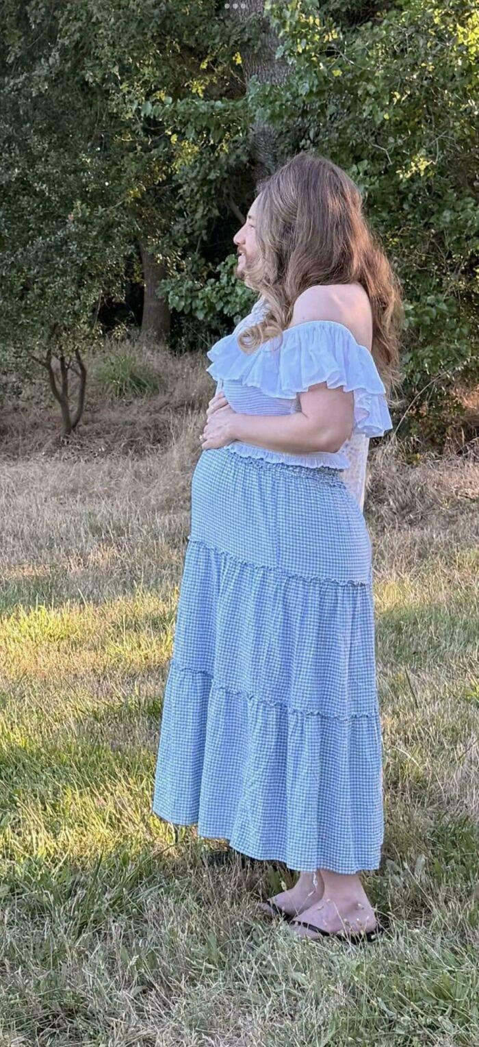 A pregnant woman in a white ruffled top and blue gingham skirt poses in a field, looking like a glitch in the matrix.