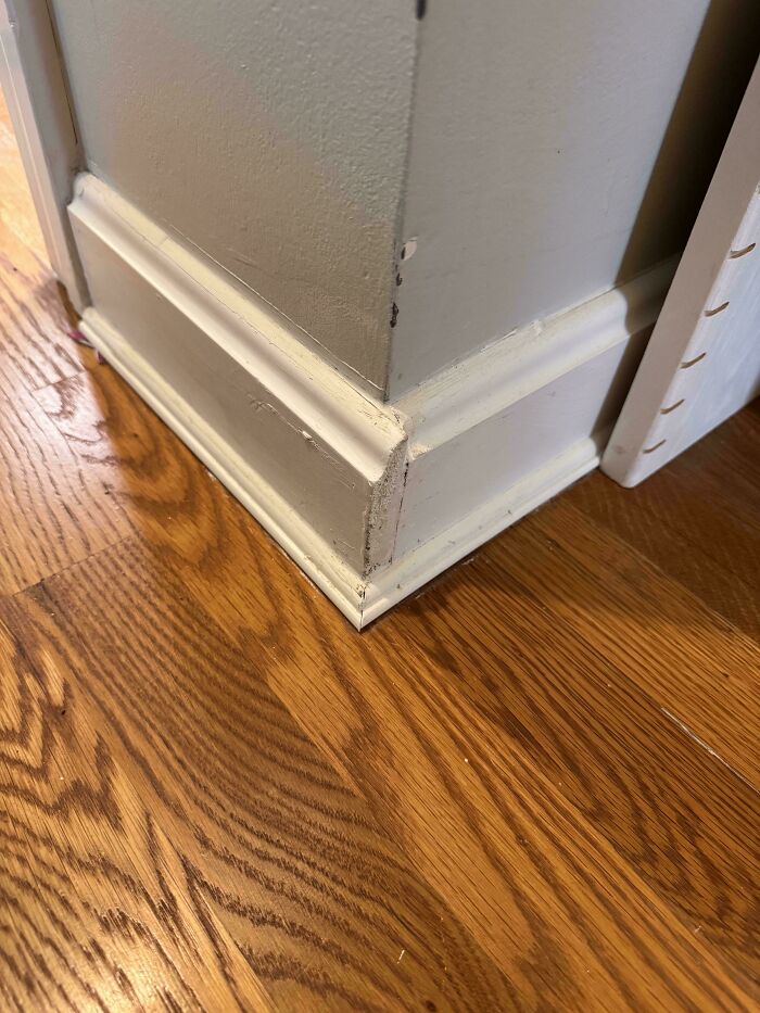 A questionable DIY project showcasing poorly aligned baseboard molding on a home wall corner.