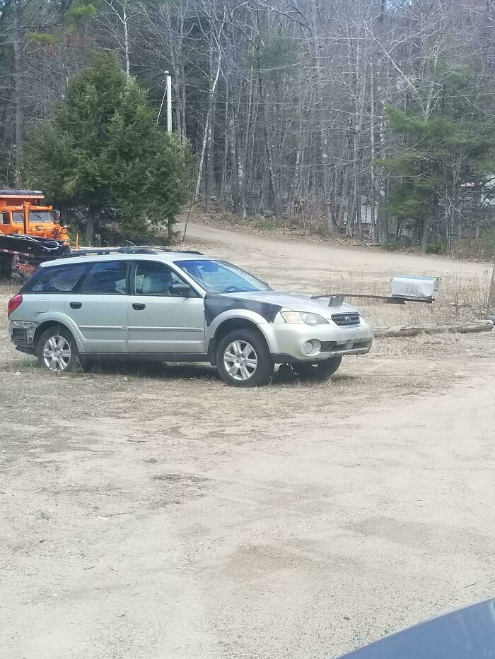 A questionable DIY project showing a silver station wagon car parked near a woodland road with a front hood mod.