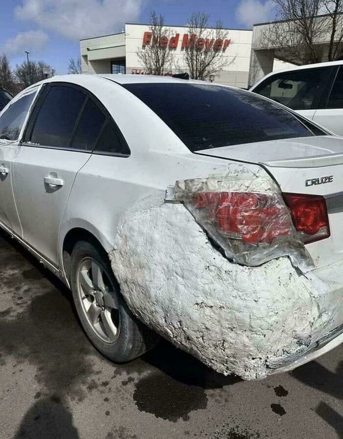 A questionable DIY project featuring a car with its rear bumper poorly repaired with spray foam and tape.