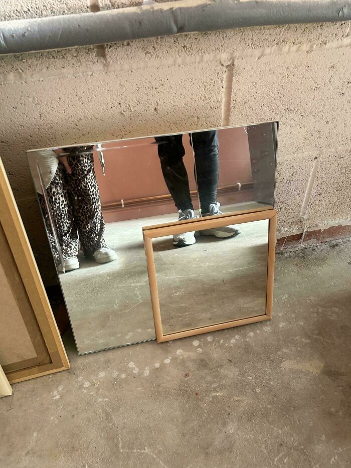 A questionable DIY mirror project with a smaller framed mirror attached to a larger one on a concrete floor.