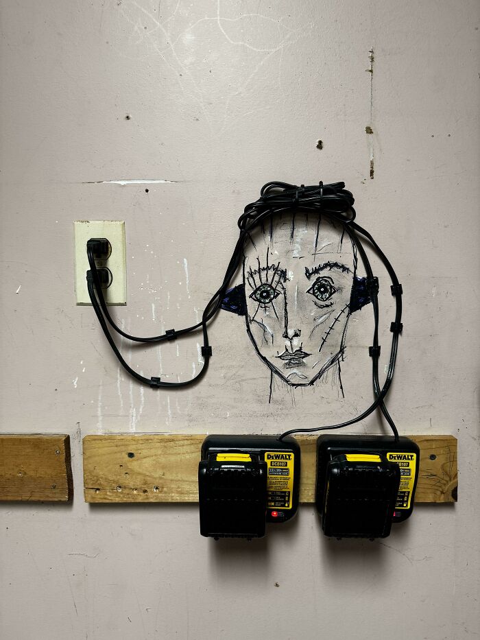 Black power cords arranged around a face drawing on a wall in a questionable DIY project