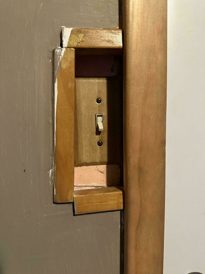 A poorly fitted wooden frame around a wall light switch, highlighting questionable DIY projects.