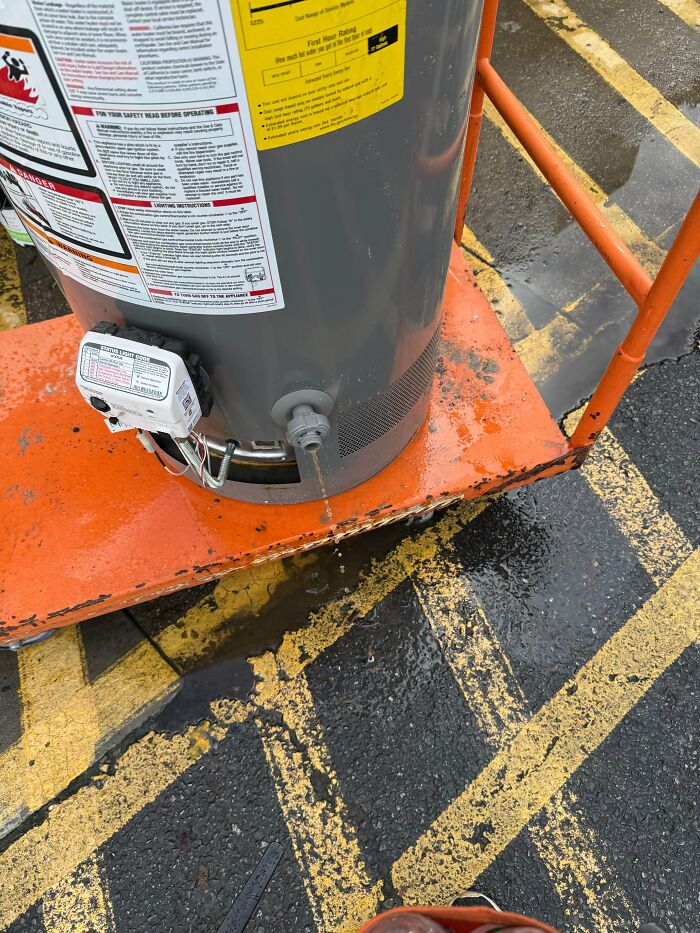 A leaking grey water heater on an orange cart, a frustrating scene for homedepot employees