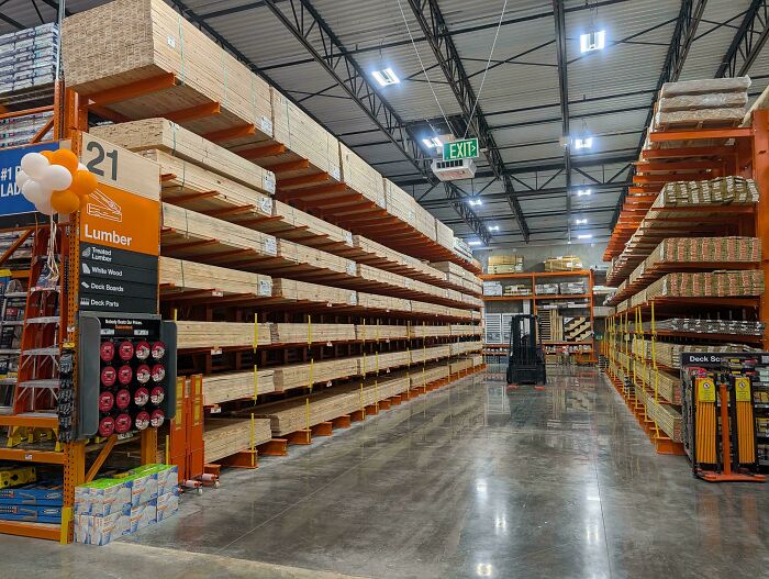 A wide lumber aisle inside a home depot store with organized wooden planks on shelves