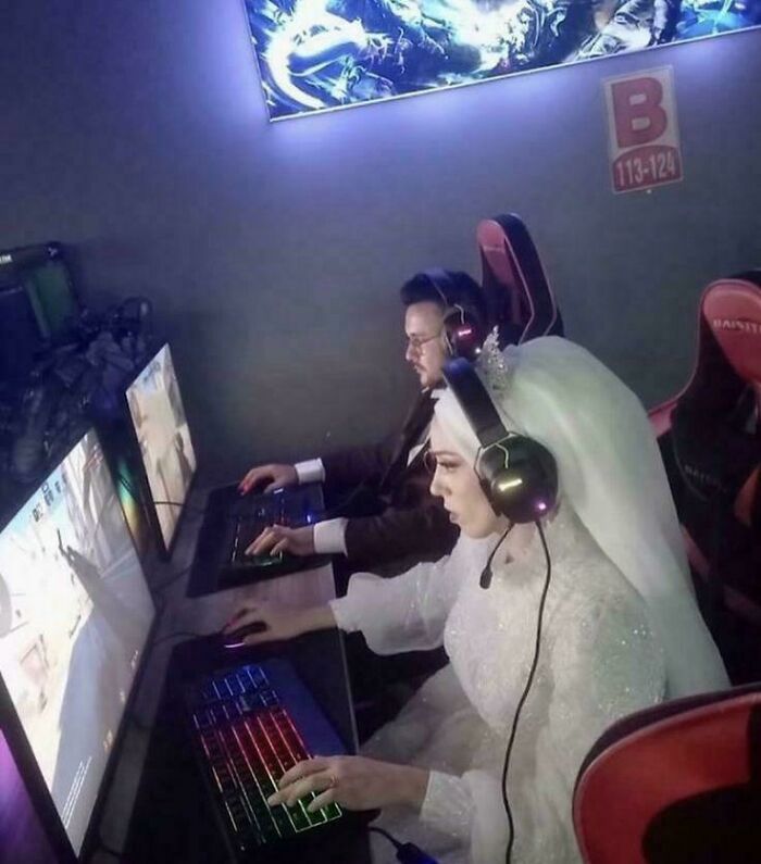 A newlywed couple in a wedding dress and suit gaming together at computers, a peculiar real life moment shared online.
