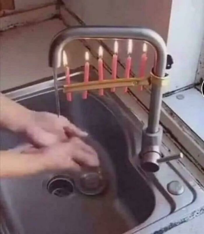A peculiar scene of hands washing in a sink, with lit candles attached to the faucet.